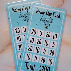 May include: A blue and white card with a cartoon cloud design and the text "Rainy Day Fund". The card has a grid with numbers 5, 10, and 20. The total amount is $200.