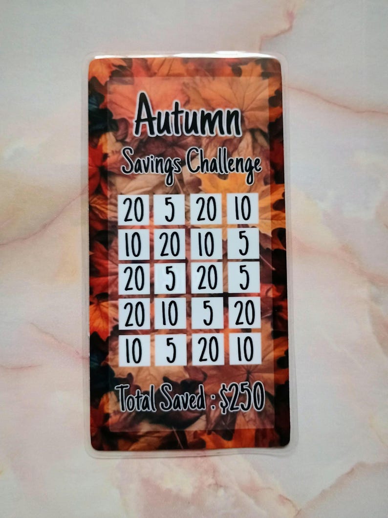 May include: A savings challenge card with a fall theme. The card has a grid of numbers, including 5, 10, and 20. The card also has the text "Autumn Savings Challenge" and "Total Saved: $250".