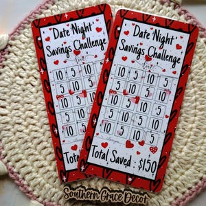 May include: Two red and white cards with a date night savings challenge. The cards have a grid of numbers with hearts and the text "Date Night Savings Challenge" and "Total Saved: $150".