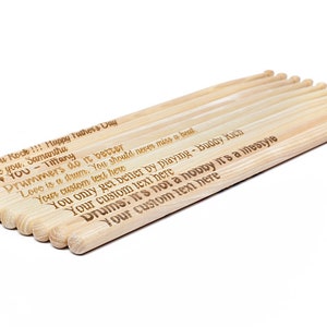 May include: A set of 10 wooden drumsticks with personalized messages engraved on them. The messages include "Dad, you Rock!!! Happy Father's Day", "I love you. Samantha", "I &hearts; YOU - Tiffany", "Drummers do it better", "Love is a drum. You should never miss a beat.", "Your custom text here", "You only get better by playing - Buddy Kich", "Your custom text here", "Drums: it's not a hobby it's a lifestyle", "Your custom text here".