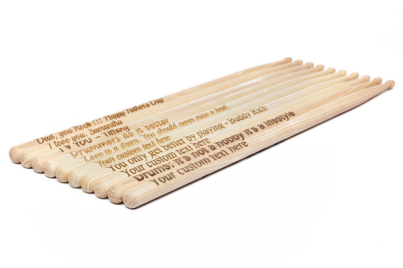May include: A set of 10 wooden drumsticks with personalized messages engraved on them. The messages include "Dad, you Rock!!! Happy Father's Day", "I love you. Samantha", "I &hearts; YOU - Tiffany", "Drummers do it better", "Love is a drum. You should never miss a beat.", "Your custom text here", "You only get better by playing - Buddy Kich", "Your custom text here", "Drums: it's not a hobby it's a lifestyle", "Your custom text here".