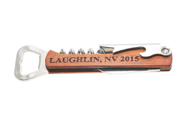 May include: A wooden wine opener with a silver bottle opener, corkscrew, and foil cutter. The handle is engraved with the text "Laughlin, NV 2015".