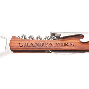 May include: A wooden bottle opener with a corkscrew and a bottle cap opener. The handle is engraved with the text "GRANDPA MIKE".