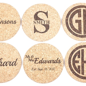 May include: A collection of six round cork coasters. Each coaster features custom text in a dark brown font. The text includes names, initials, and a wedding date. The coasters are made of natural cork material.