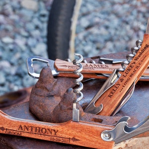 May include: Three wooden bottle openers with engraved text. The top opener says "Kelly & Luke's Wedding...Long Beach, CA." The middle opener says "James, Groomsman." The bottom opener says "Anthony, Groom 10-20-2015."