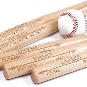 May include: A baseball and several wooden baseball bats. The bats are engraved with names and the date 10-25-2017, with titles such as "Father of the Bride", "Groomsman", and "Best Man". The baseball has red stitching.