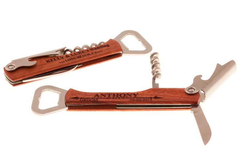 May include: Two wooden multi-tools with engraved text. The top tool has a bottle opener, corkscrew, and a small knife. The bottom tool has a bottle opener, a corkscrew, and two small knives. The top tool is engraved with "KELLY & LUKE'S Wedding *** LONG BEACH, CA ***". The bottom tool is engraved with "ANTHONY GROOM 10-20-2015".