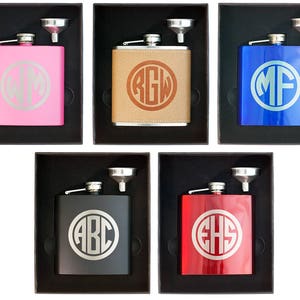 May include: Five different color stainless steel hip flasks with a funnel and a monogrammed circle on the front. The flasks are in black boxes with a white background.