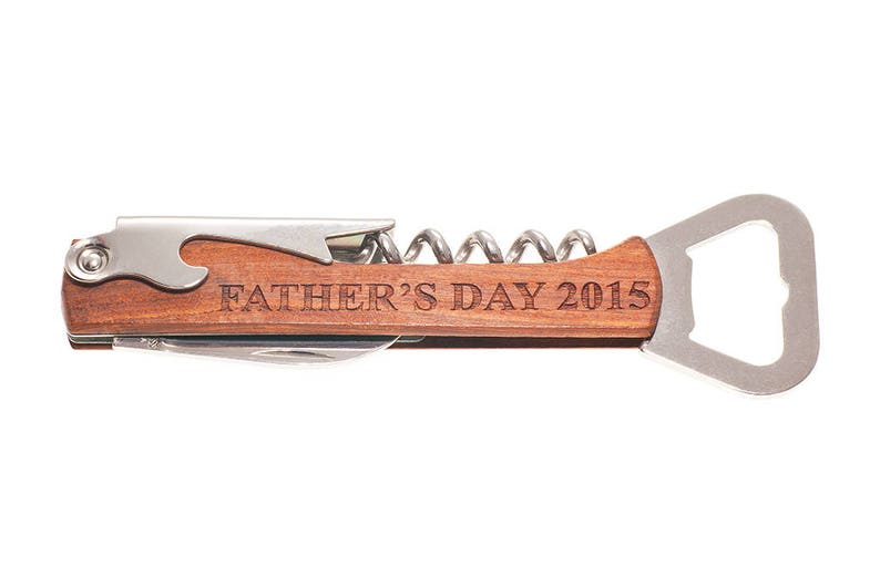 May include: A wooden handled bottle opener with a corkscrew and a bottle opener. The handle is engraved with the text "Father's Day 2015".