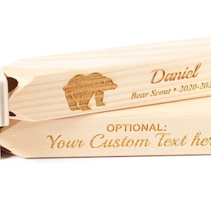 May include: Wooden whistle with a bear design and the text "Daniel Bear Scout 2020-2021". The bottom of the whistle has the text "OPTIONAL: Your Custom Text here".