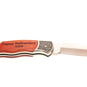 Puede incluir: Un cuchillo de bolsillo plateado con mango de madera grabado con "Happy Retirement 12/16/15".
