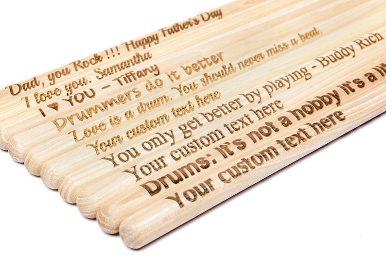 May include: A set of wooden drumsticks with personalized messages engraved on them. The messages include "Dad, you Rock!!! Happy Father's Day", "I love you. Samantha", "I &hearts; YOU - Tiffany", "Drummers do it better", "Love is a drum. You should never miss a beat.", "Your custom text here", "You only get better by playing - Buddy Rich", "Your custom text here", "Drums: It's not a hobby it's a", "Your custom text here".