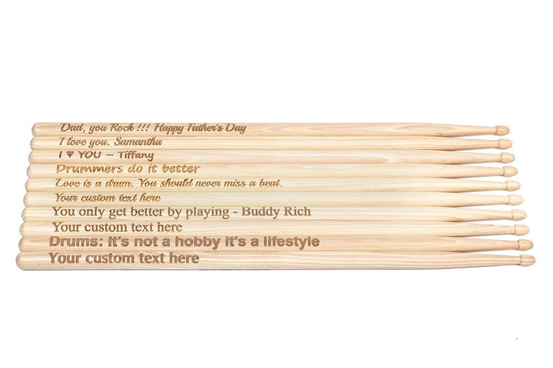 May include: A set of wooden drumsticks with personalized engravings. The text reads "Dad, you Rock!!! Happy Father's Day", "I love you. Samantha", "I YOU - Tiffany", "Drummers do it better", "Love is a drum. You should never miss a beat.", "Your custom text here", "You only get better by playing - Buddy Rich", "Your custom text here", "Drums: It's not a hobby it's a lifestyle", "Your custom text here".