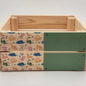 May include: A wooden storage box with a green painted top and bottom. The sides are decorated with a pattern of colourful dinosaurs.