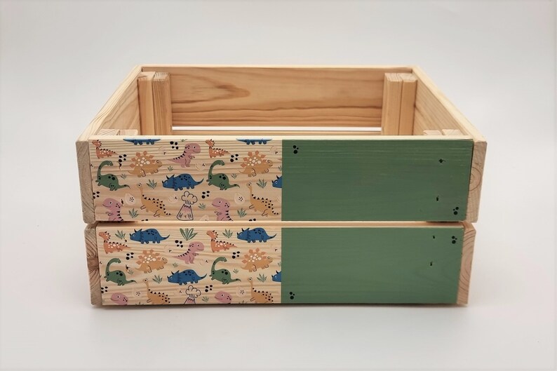 May include: A wooden storage box with a green painted top and bottom. The sides are decorated with a pattern of colourful dinosaurs.