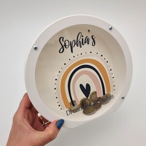 May include: White wooden piggy bank with a clear plastic window. The window shows a rainbow design with a heart and the text "Sophia's Dreamcatcher Wishes".