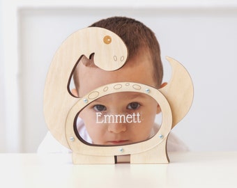 May include: A wooden dinosaur piggy bank with a slot for coins. A young boy is looking through the slot, and his name "Emmett" is written on the bank.