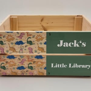 Close-up of a wooden kids' book storage box with colorful dinosaur prints and a custom name. Perfect for book lovers and toy storage.