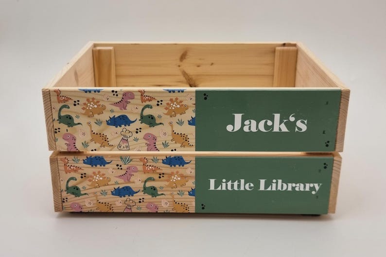 Close-up of a wooden kids' book storage box with colorful dinosaur prints and a custom name. Perfect for book lovers and toy storage.