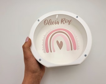 May include: White wooden round box with a pink and brown rainbow and a heart design. The box has the name "Olivia Rose" written on it.