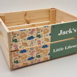 Wooden book storage crate with a dinosaur theme, featuring a personalized name panel. Ideal for kids’ rooms, nursery decor, and book organization.