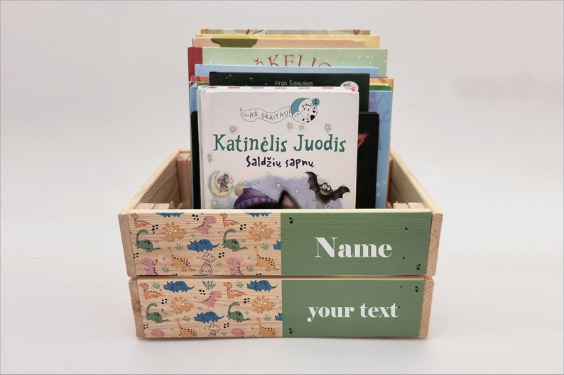 May include: A wooden crate with a green and dinosaur print design. The crate is filled with children's books. The front of the crate has a green panel with the text "Name your text".