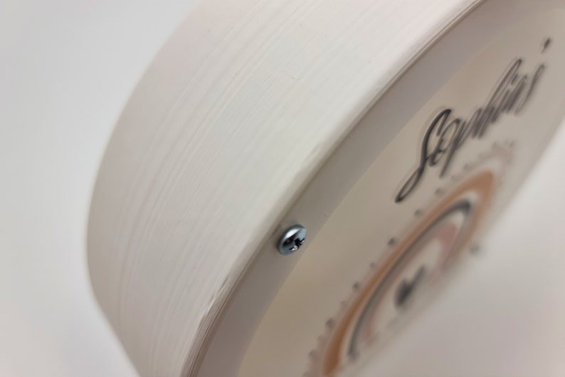 May include: A white wooden round sign with a clear plastic overlay. The overlay features a rainbow design with the name "Sophia's" written in black cursive.
