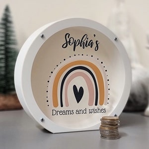 May include: White wooden piggy bank with a rainbow and heart design. The text "Sophia's Dreams and Wishes" is printed on the front.