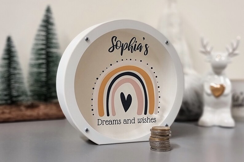 May include: White wooden piggy bank with a rainbow and heart design. The text "Sophia's Dreams and Wishes" is printed on the front.