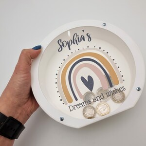 May include: White wooden piggy bank with a rainbow design and the text "Sophia's Dreams and wishes".