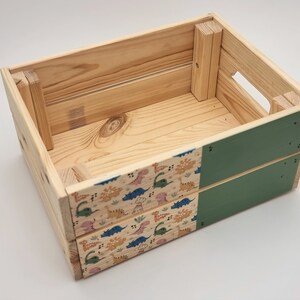 May include: A wooden crate with a green painted bottom and a dinosaur pattern on the sides. The crate is empty.
