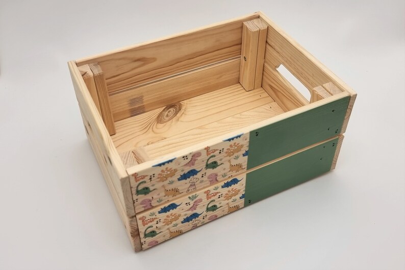 May include: A wooden crate with a green painted bottom and a dinosaur pattern on the sides. The crate is empty.