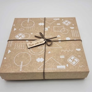 May include: A brown cardboard gift box with a geometric pattern in white. The box is tied with brown twine and has a wooden tag that says "Made with love".