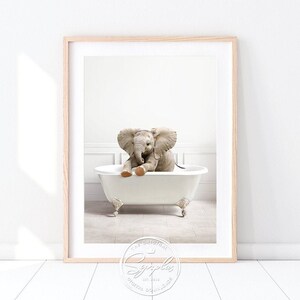 Könnte beinhalten: Gerahmter Druck eines Baby-Elefanten in einer weißen Badewanne mit Löwenfüßen. Der graue Elefant hat große Ohren. Der Druck ist in einem hellen Holzrahmen. Digitaler Download.