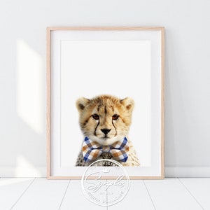 May include: A cute cheetah cub wearing a blue and brown bow tie. The cheetah is looking directly at the camera. The background is white.