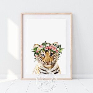 Könnte beinhalten: Ein süßes Tigerjunges mit einer rosa und weißen Blumenkrone. Der Tiger hat braune und orange Streifen und blaue Augen. Der Hintergrund ist weiß.