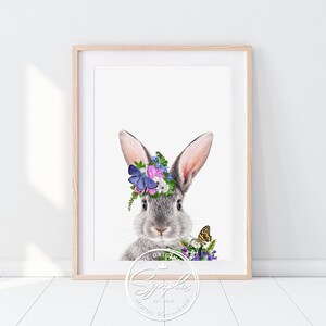 Könnte beinhalten: Ein graues Kaninchen mit einer Blumenkrone und einem Schmetterling auf dem Kopf. Das Kaninchen schaut direkt in die Kamera. Der Hintergrund ist weiß.