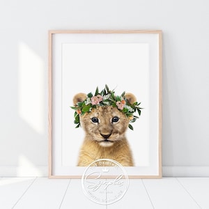 Könnte beinhalten: Ein süßes Löwenjunges trägt eine Blumenkrone mit rosa und weißen Blüten. Das Löwenjunges schaut mit einem süßen Ausdruck in die Kamera. Der Hintergrund ist weiß.