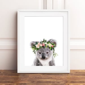 May include: A cute koala wearing a flower crown with pink, white, and green flowers. The koala is looking directly at the camera.