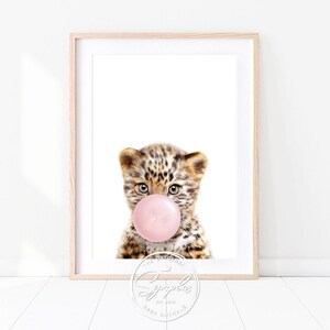 Könnte beinhalten: Ein süßes Leopard-Junges mit einem rosa Kaugummi im Maul. Das Junge schaut mit einem verspielten Ausdruck in die Kamera. Der Hintergrund ist weiß.