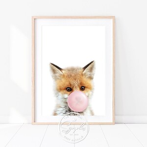 Könnte beinhalten: Ein süßes Füchschen mit einem rosa Kaugummi im Maul. Der Fuchs schaut direkt in die Kamera. Der Hintergrund ist weiß.