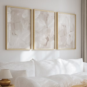 May include: A white sectional sofa with two white accent chairs in a living room with a large window, a wooden coffee table, and three gold candle holders.