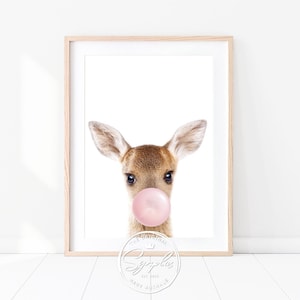 Könnte beinhalten: Ein Kitz mit großen Ohren bläst eine rosa Blase. Das Kitz schaut direkt in die Kamera. Der Hintergrund ist weiß. Das Bild hat unten ein Logo mit der Aufschrift "The Original Sygplus Est. 2015 Baby Animals".
