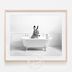 Könnte beinhalten: Schwarz-Weiß-Druck in einem Rahmen, der einen Esel in einer weißen Badewanne mit Löwenfüßen und einer kleinen Ente zeigt. Der Esel ist grau und weiß, und die Ente ist weiß. Der Rahmen ist aus hellem Holz.