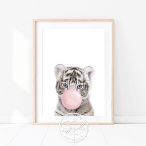 Könnte beinhalten: Ein weißes Tigerjunges mit blauen Augen bläst eine rosa Blase. Das Bild ist mit einem hellen Holzrahmen gerahmt. Der Text "The Original" und "Baby Animals" ist in der unteren rechten Ecke sichtbar.