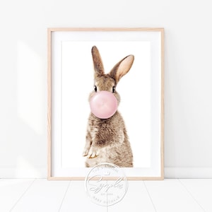 Könnte beinhalten: Ein braunes Kaninchen mit rosa Ohren bläst eine rosa Blase. Das Kaninchen schaut direkt in die Kamera. Der Hintergrund ist weiß.
