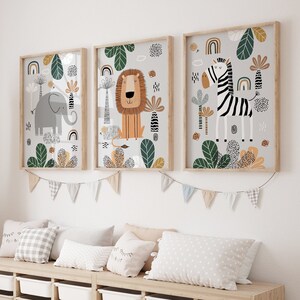 May include: Three framed illustrations of animals in a jungle setting. The illustrations feature a lion, an elephant, and a zebra. The frames are light wood and the illustrations are on a white background.