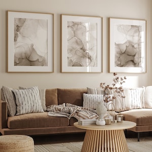 Puede incluir: Un sof&aacute; seccional marr&oacute;n con una manta de tiro marr&oacute;n claro y varias almohadas estampadas. El sof&aacute; est&aacute; en una sala de estar con una mesa de caf&eacute; de madera y tres impresiones de arte abstracto enmarcadas en la pared.