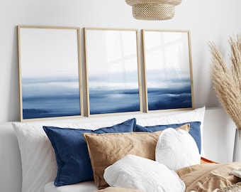 May include: Three framed abstract paintings with a blue watercolour gradient design. The paintings are hung above a bed with white and brown pillows.