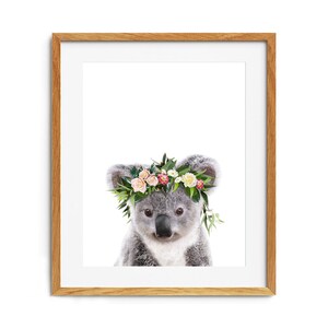 May include: A cute koala wearing a flower crown with pink, white, and yellow flowers. The koala is looking directly at the camera.